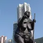 Survival of the Fattest bronze sculpture showing a large woman carrying scales and a staff on the shoulders of an emaciated figure.