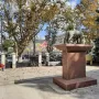 Capitoline Wolf sculpture with Romulus and Remus on a tall red-stone pedestal in an urban square.