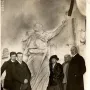 A group of five people stands around a large sculpture of Mickiewicz in a workshop, with other busts and reliefs on the walls.