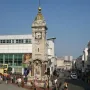 Brighton Clock Tower standing in a busy city plaza with pedestrians, a red double-decker bus, and a street beside it.