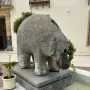 Stone elephant fountain standing on a granite base with water flowing from its trunk into a shallow basin.