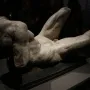 Reclining River God sculpture with a textured torso and legs on a dark base.
