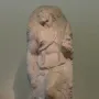Unfinished marble sculpture of Saint Matthew emerging from stone, with a bearded figure looking upward.