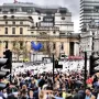 The blue Hahn/Cock sculpture stands on a pedestal in Trafalgar Square with a large crowd nearby.