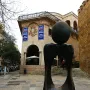 Monument a la dona by Joan Miró, a dark abstract sculpture with a sphere on a curved base in front of a historic stone building.