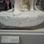 Close-up of The First Funeral sculpture showing the carved inscription and several bare feet on the plaster base.