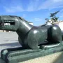 The Leona de Baena sculpture in green metal, shown in profile on a stone base in a town square.