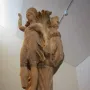 Dancers of Delphi sculpture showing two draped female figures with raised arms around a central pillar on an ornate base.