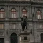 El Caballito, a dark equestrian statue on a stone pedestal, with a grand stone building in the background.