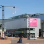 Marshal Mannerheim equestrian statue in front of a modern glass building in Helsinki, with a pedestrian in the foreground.