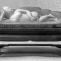 Doctor\'s Lady, a light-colored female figure reclining on a small couch with a patterned cushion, shown on a wooden stand.