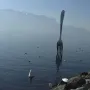 The Fork of Vevey sculpture rises from the water with mountains and birds in the background.