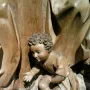 Wooden sculpture of Saint Luke as a curly-haired child kneeling with one hand extended.