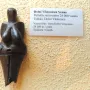 Venus of Dolní Věstonice figurine with prominent breasts and a rounded belly, displayed beside a multilingual label.