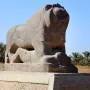 The Lion of Babylon stone sculpture resting on a base beneath a clear blue sky.