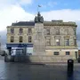 Paisley War Memorial stone cenotaph in a town square with carved details and dark figures on top.