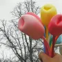 Bouquet of Tulips sculpture with a hand holding pink, yellow, and red tulips against bare tree branches and an overcast sky.