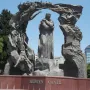 Huseyn Javid monument with a central robed figure, flanked by tall sculptural forms and arching figures above a red stone base.