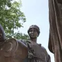 Detail of Alma Mater showing the woman’s face, braided hair, patterned bodice, and a bronze scroll with an arm resting on it.