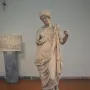 Marble statue of Armed Aphrodite standing in flowing drapery with her head bowed, showing wear and damage.