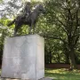 Bernardo de Gálvez equestrian statue on a tall stone pedestal surrounded by trees.