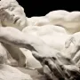 Avarice and Lust by Auguste Rodin, a cream-colored sculpture of two intertwined nude figures against a dark background.