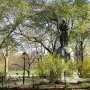 Seventh Regiment Memorial statue on a tall stone pedestal in Central Park, seen from behind among trees and shrubs.