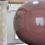 Large Red Sphere sculpture on a two-tiered circular pedestal in a bright interior space.