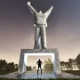 Monument to Stjepan Filipović, a tall abstract concrete statue with raised arms above a lit pedestal arch and silhouetted figure.