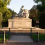 The Strasbourg War Memorial, a large stone sculpture of figures in a mournful embrace on a tiered pedestal, surrounded by grass, bushes, and autumn trees.