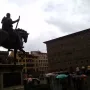 Cosimo I Equestrian Monument seen from behind in a wet Florence square with umbrellas and a Generali building in the background.