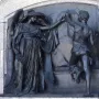Death and the Sculptor bronze relief showing a winged woman reaching toward a sculptor with an implement.