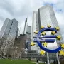 Blue euro sculpture with yellow stars in front of Frankfurt skyscrapers and a cloudy sky.