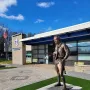 The Ideal Scout bronze statue on a stone pedestal outside a modern building with a blue sign and American flag.